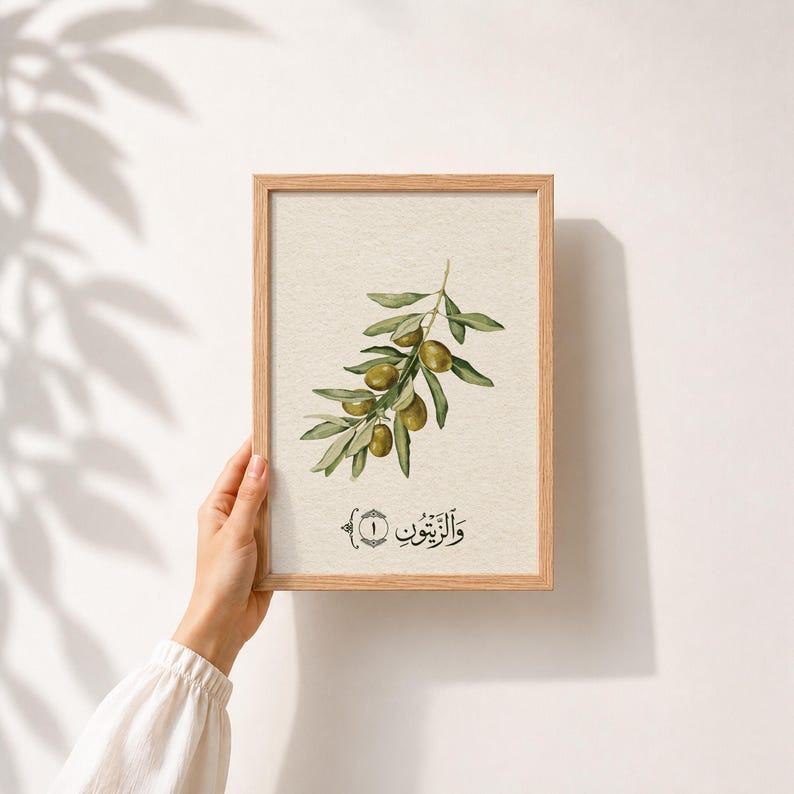 May include: A rectangular wooden frame containing a print of an olive branch with green leaves and olives on a cream background. Below the branch is the Arabic text "وَالزَّيْتُونِ" with the number one inside a circular decorative border.