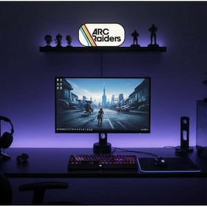 May include: A gaming setup with a computer monitor displaying a futuristic cityscape. A keyboard, mouse, and mousepad are on the desk. The wall features a shelf with figurines and a sign that reads "ARC Raiders". The room is illuminated with purple lighting.