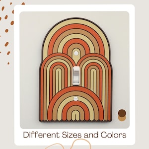 May include: A decorative light switch cover with a retro design. The cover features a series of arched shapes in shades of orange, tan, and brown, with a white switch in the center. The text "Different Sizes and Colors" is at the bottom.