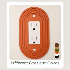 May include: An orange electrical outlet cover with a layered, oval design. The cover surrounds a white outlet with two sockets. The image includes the text "Different Sizes and Colors" and a colour palette of brown, green, orange, and black.