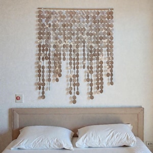 Puede incluir: Decoración mural compuesta por numerosos discos pequeños y redondos con aspecto metálico. Los discos están ensartados en filas verticales, creando un efecto de cascada. Cuelga sobre una cama con almohadas blancas.