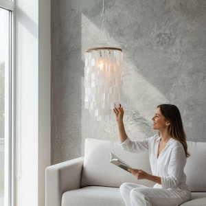 May include: A cylindrical pendant light fixture featuring multiple tiers of translucent white capiz shell squares suspended from a circular frame wrapped in natural jute rope, hanging from a single white cord with a central light bulb.