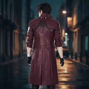 Może przedstawiać: Bordowy skórzany płaszcz z wysokim kołnierzem i ozdobnymi przeszyciami. Płaszcz ma dwurzędowy krój, paski na ramionach i rękawy zapinane na zamek. Osoba ma na sobie czarne rękawiczki i stoi na ulicy.