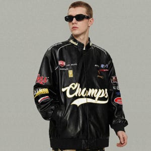 May include: Black leather jacket with white and yellow embroidered details. The jacket features the word "Champs" in large script across the front, along with various patches and logos. The jacket has a ribbed collar and cuffs.