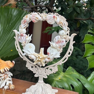 Espejo de tocador artesanal con forma de concha marina: forma de corazón, decoración costera, perlas y detalles de estrella de mar.