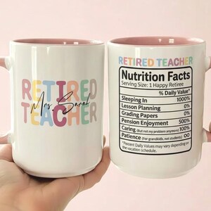 K&ouml;nnte beinhalten: Wei&szlig;er Keramikbecher mit rosa Griff und Innenraum. Der Becher tr&auml;gt den Text "RETIRED TEACHER" in bunten Buchstaben, darunter "Mrs. Sarah". Die andere Seite hat ein "Nutrition Facts"-Etikett f&uuml;r einen gl&uuml;cklichen Rentner.