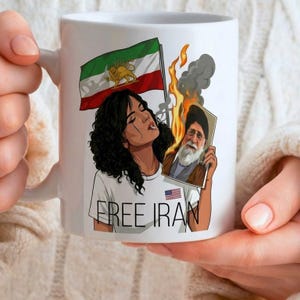 Puede incluir: Taza de cerámica blanca con un diseño de una mujer con cabello negro rizado, sosteniendo una foto en llamas y una bandera iraní. El texto "FREE IRAN" está impreso en la camiseta de la mujer, con una pequeña bandera estadounidense. La taza tiene un asa blanca.