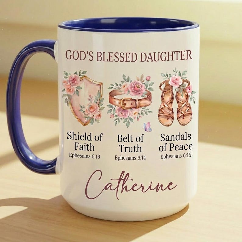 May include: White ceramic mug with a blue handle and interior rim. The mug features the text "GOD'S BLESSED DAUGHTER" and illustrations of a shield, belt, and sandals, with the name "Catherine" in script.
