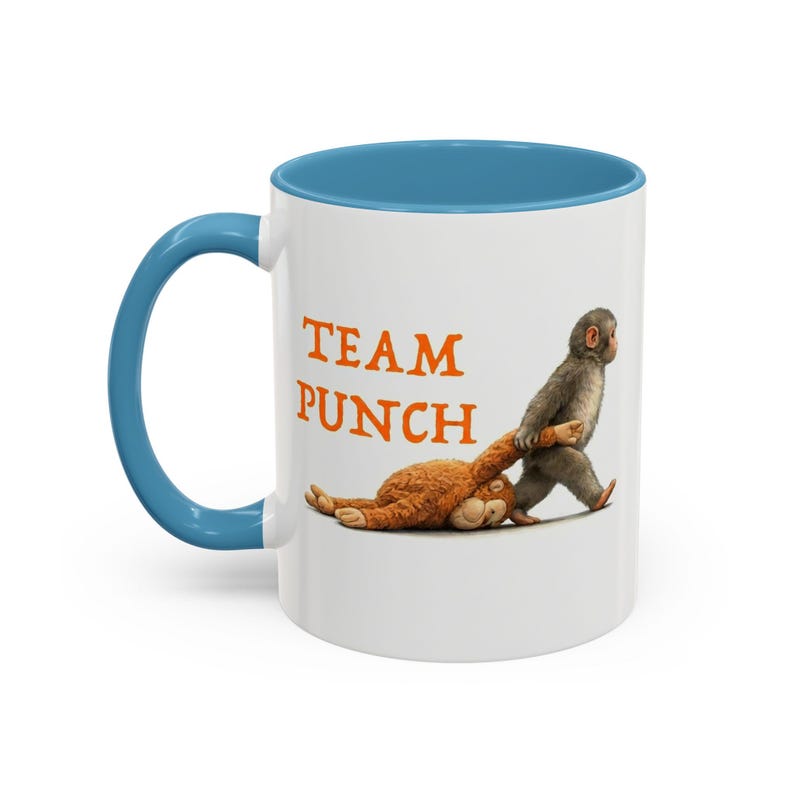 May include: White ceramic mug with a blue interior and handle. The mug features the text "TEAM PUNCH" in orange letters, along with an illustration of a monkey dragging a stuffed animal.