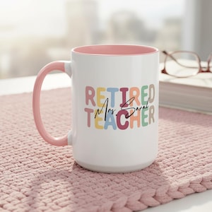 K&ouml;nnte beinhalten: Wei&szlig;er Keramikbecher mit rosa Innenraum und Griff. Der Becher zeigt den Text "RETIRED Mrs. Sarah TEACHER" in bunten Blockbuchstaben. Der Becher steht auf einer rosa geh&auml;kelten Oberfl&auml;che.
