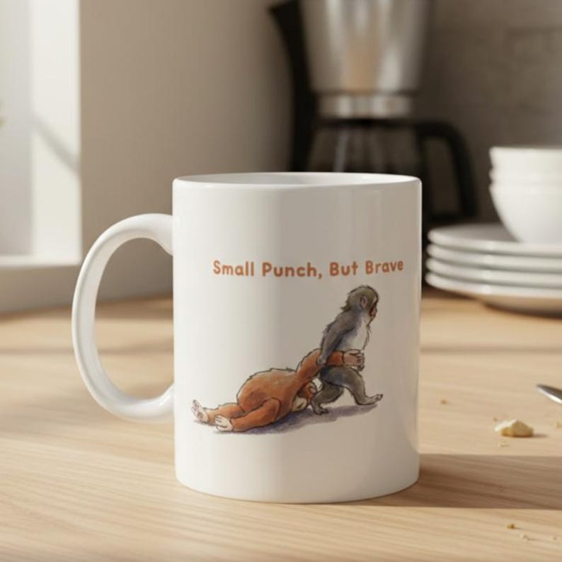 May include: White ceramic mug with a humorous illustration of two monkeys and the text "Small Punch, But Brave". The mug has a large, curved handle and is suitable for hot or cold beverages.