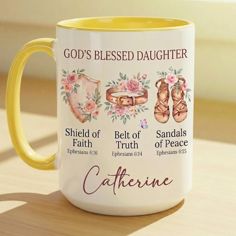 May include: White ceramic mug with a yellow handle and interior. The mug features the text "GOD'S BLESSED DAUGHTER" and illustrations of a shield, belt, and sandals, with the name "Catherine" at the bottom.