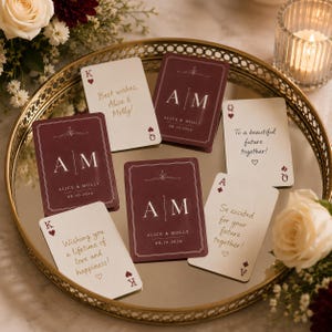 May include: A set of custom playing cards featuring a deep burgundy and white color scheme. The cards display the initials A and M, the names Alice and Molly, and the date 08.10.2026, alongside various handwritten-style messages of well wishes.