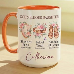 May include: White ceramic mug with an orange handle and interior. The mug features the text "GOD'S BLESSED DAUGHTER" and illustrations of a shield, belt, and sandals, with the name "Catherine" at the bottom. Floral accents and scripture references are also included.