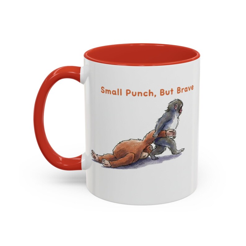 May include: White ceramic mug with a red interior and handle. The mug features an illustration of two cartoon animals, one brown and one gray, with the text "Small Punch, But Brave".