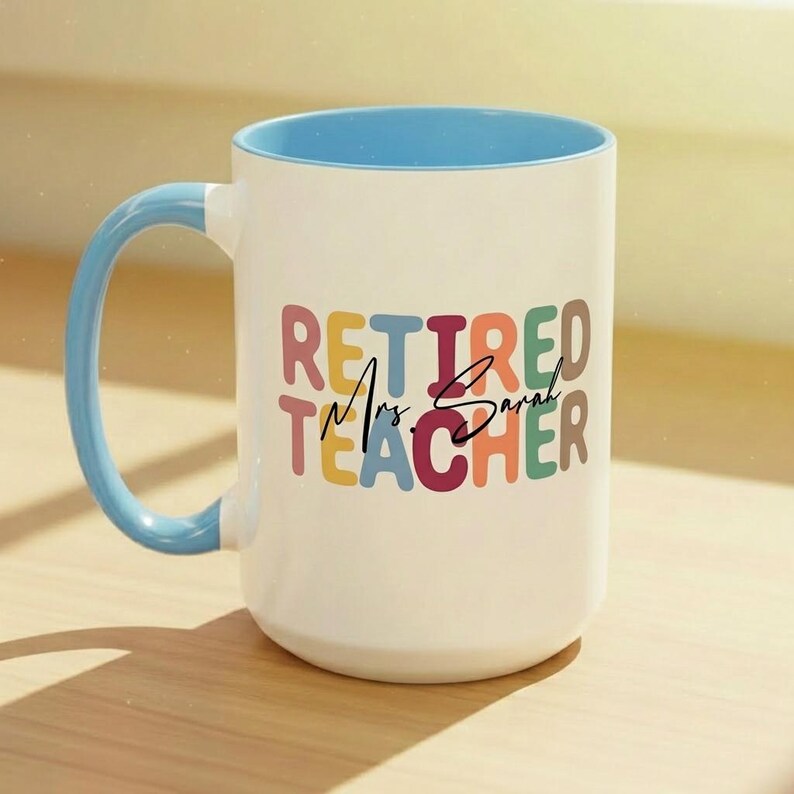K&ouml;nnte beinhalten: Wei&szlig;er Keramikbecher mit blauem Innenraum und Henkel. Der Becher zeigt den Text "Retired Mrs. Sarah Teacher" in bunten Buchstaben. Ein perfektes Geschenk f&uuml;r eine pensionierte Lehrerin.