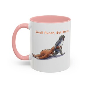 May include: White ceramic mug with a pink interior and handle. The mug features an illustration of two cartoon monkeys, one brown and one gray, in a playful wrestling pose. The text "Small Punch, But Brave" is printed on the mug.