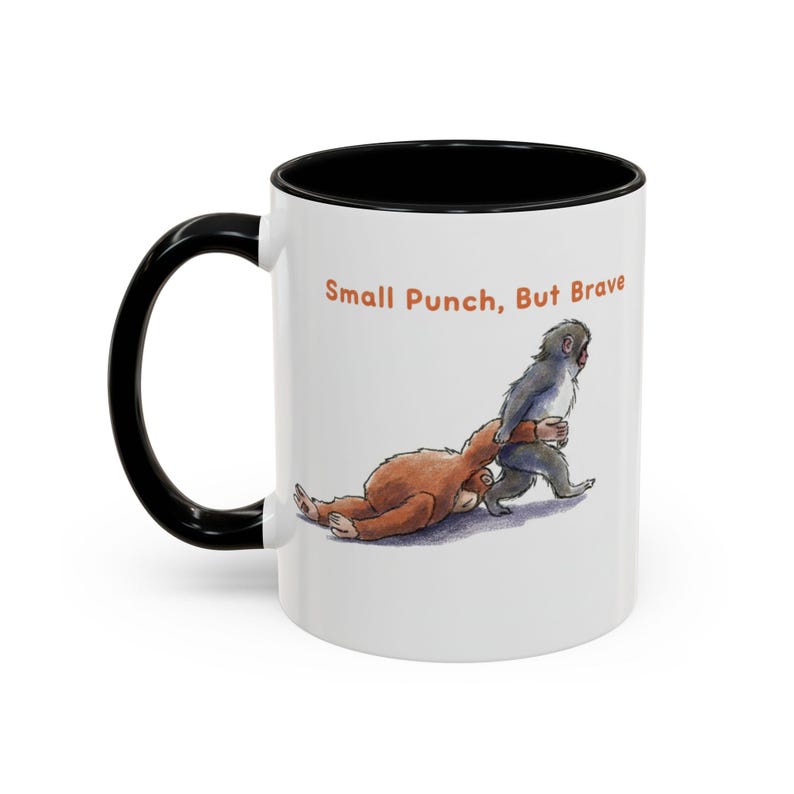 May include: White ceramic mug with a black handle and interior. The mug features an illustration of two cartoon monkeys, one brown and one gray, in a playful fighting pose. The text "Small Punch, But Brave" is printed above the illustration.