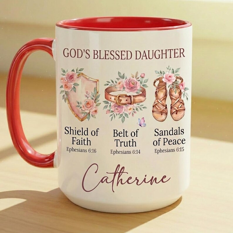 May include: White ceramic mug with a red handle and interior. The mug features the text "GOD'S BLESSED DAUGHTER" and illustrations of a shield, belt, and sandals, along with the name "Catherine".