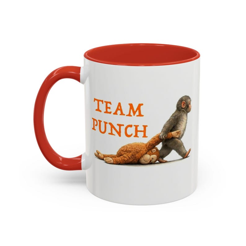 May include: White ceramic mug with a red interior and handle. The mug features the text "TEAM PUNCH" in orange letters, along with an illustration of a monkey dragging a stuffed animal. A fun and unique gift idea.