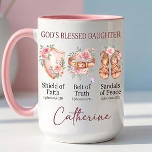 May include: White ceramic mug with a pink handle and interior. The mug features the text "GOD'S BLESSED DAUGHTER" and the name "Catherine". It also displays illustrations of a shield, belt, and sandals, with related text from Ephesians.