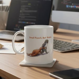 May include: White ceramic mug with the text "Small Punch, But Brave" and a cartoon illustration of two animals. One animal is on the ground, and the other is standing and holding the other animal. The mug is on a square coaster.