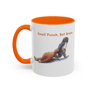 May include: White ceramic mug with an orange interior and handle. The mug features a cartoon illustration of two animals, with the text "Small Punch, But Brave" in orange letters.