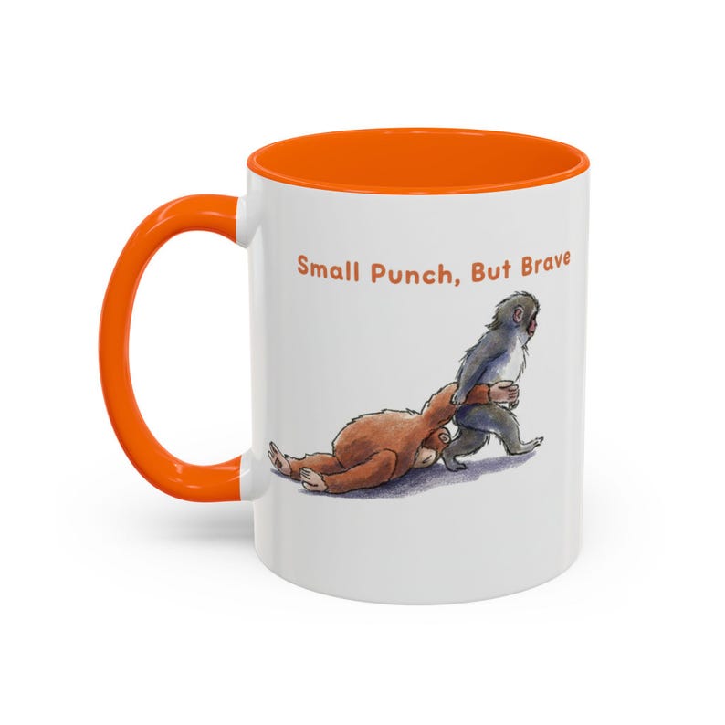 May include: White ceramic mug with an orange interior and handle. The mug features a cartoon illustration of two animals, with the text "Small Punch, But Brave" in orange letters.