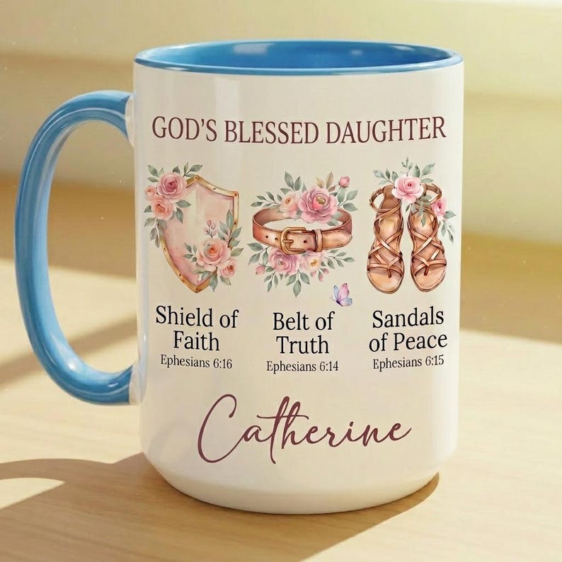 May include: White ceramic mug with a blue handle and interior rim. The mug features the text "GOD'S BLESSED DAUGHTER" and illustrations of a shield, belt, and sandals, with the name "Catherine" at the bottom.