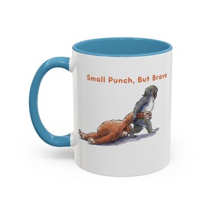 May include: White ceramic mug with a blue interior and handle. The mug features an illustration of two cartoon monkeys, one brown and one gray, with the text "Small Punch, But Brave" in orange.