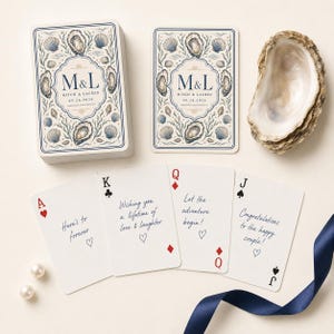 Pu&ograve; includere: Un mazzo di carte da gioco personalizzato con un'illustrazione nautica di ostriche e conchiglie, con il testo M&L, Mitch & Lauren e 09.26.2026. Quattro carte singole mostrano messaggi come Here's to forever, accanto a un guscio d'ostrica.