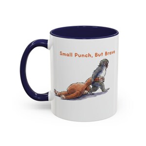 May include: White ceramic mug with a navy blue interior and handle. The mug features an illustration of two cartoon animals, with the text "Small Punch, But Brave" in orange.
