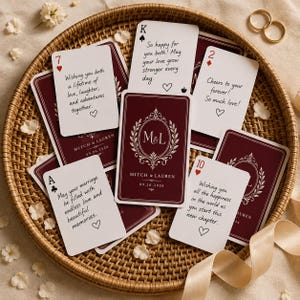Peut inclure: Un jeu de cartes à jouer personnalisées dans un plateau rond en osier. Les cartes présentent un dos bordeaux profond avec un motif de couronne de laurier blanc, les initiales M&L et la date 09.26.2026. Plusieurs cartes portent des messages.
