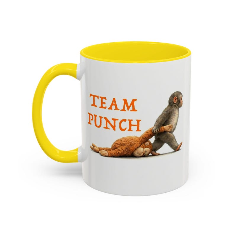 May include: White ceramic mug with a yellow interior and handle. The mug features the text "TEAM PUNCH" in orange letters. A cartoon monkey is pulling a brown stuffed animal. The mug is suitable for hot or cold beverages.
