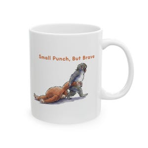 May include: White ceramic mug with a cartoon illustration of two monkeys. One monkey is pulling the other, who is lying on the ground. The text "Small Punch, But Brave" is printed above the illustration.