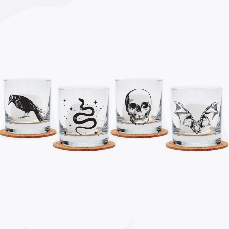May include: Set of four clear glass tumblers with cork coasters. Each tumbler features a different black and white illustration: a crow, a snake, a skull, and a bat.