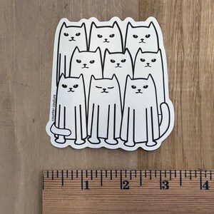 May include: A white sticker featuring a group of stylized cats with black outlines. The cats have simple facial features and are arranged in a rectangular shape. The sticker has the text "counter couture" on the left side.