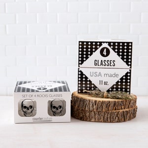 May include: Set of four 11 ounce rocks glasses with a skull design. The glasses are packaged in a black and white box with the text "Set of 4 Rocks Glasses" and "countercouture".