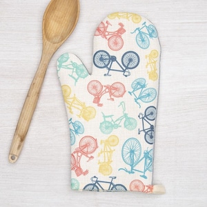 May include: A white oven mitt with a colorful bicycle pattern. The mitt has a loop for hanging and a gray trim.