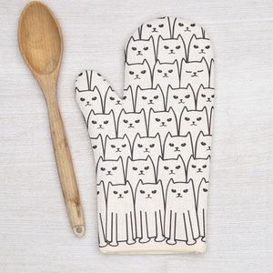 May include: A white oven mitt with a black cat pattern. The mitt is made of cotton and has a heat-resistant lining.