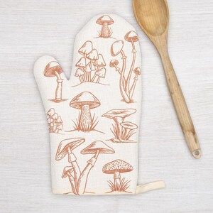 May include: A white oven mitt with a brown mushroom pattern. The mitt has a loop for hanging.