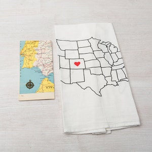 May include: A white kitchen towel with a black outline of the United States map. A red heart is in the center of the map, marking the state of Colorado.