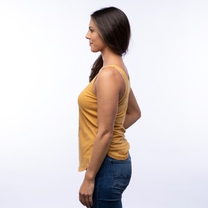 May include: A woman wearing a mustard yellow tank top and blue jeans. The tank top has a relaxed fit and a scoop neck.