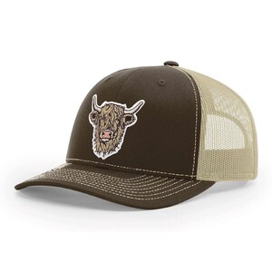 Può includere: Cappellino da camionista marrone con retro in rete beige e visiera curva. Il cappellino presenta una toppa con la testa di una mucca delle Highlands con le corna. Cuciture bianche rifiniscono la visiera e il pannello frontale.