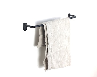 May include: A black metal towel bar mounted on a white wall with a light brown linen towel hanging from it.
