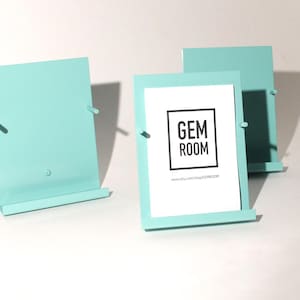 May include: Three light blue metal picture frames with a stand. The middle frame has a white card with the text "GEM ROOM" and a website address.