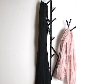May include: A black metal coat rack shaped like a tree branch with two scarves hanging from it. One scarf is black and the other is pink.