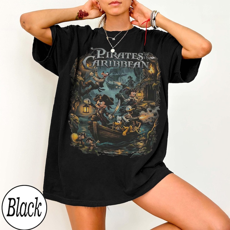 May include: Black t-shirt with a Pirates of the Caribbean graphic. The design shows cartoon characters in a pirate scene, with the words "Pirates of the Caribbean" at the top.