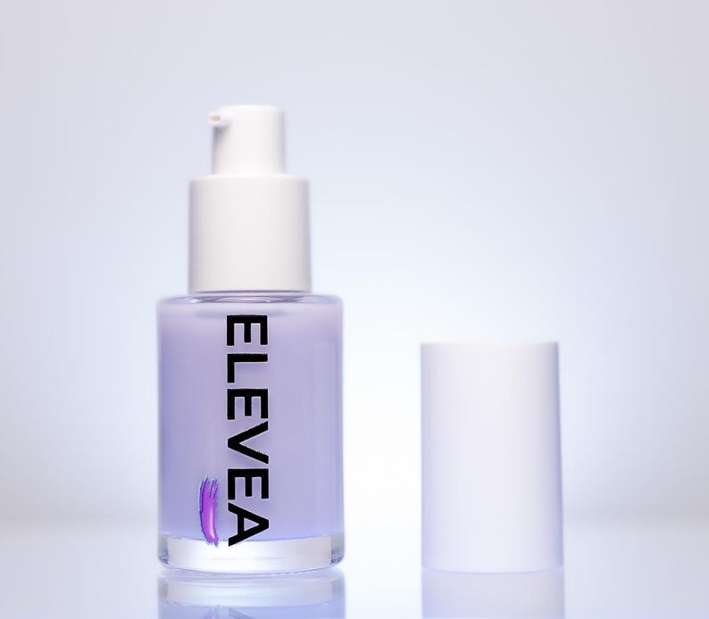 May include: A lavender-colored pump bottle with a white cap and the word "ELEVEN" printed vertically in black. A purple brushstroke design is below the text. The bottle's cap is separate, and the background is a gradient of white and light blue.