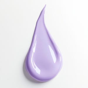 May include: A close-up of a smooth, lavender-colored cosmetic product smear against a white background. The product is in a teardrop shape, with a glossy finish and highlights.